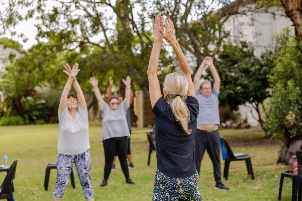 Instructor leading people over 60 in overhead arm raises during an outdoor class.