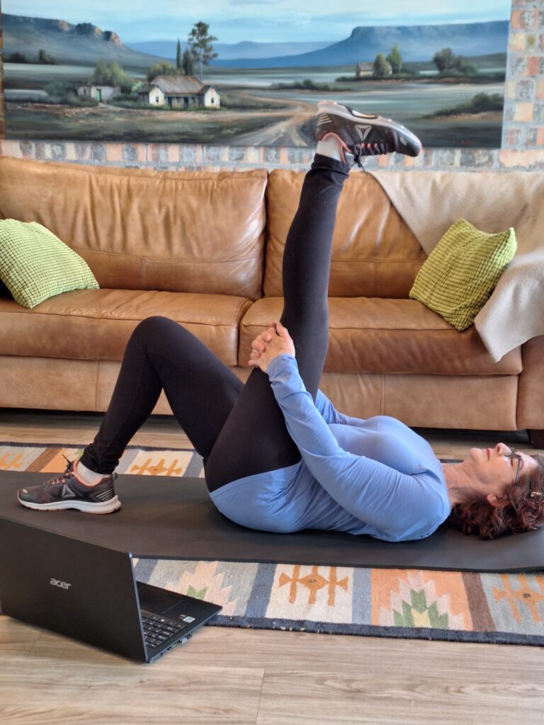 Older adult doing a hamstring stretch at home while following an online fitness class.