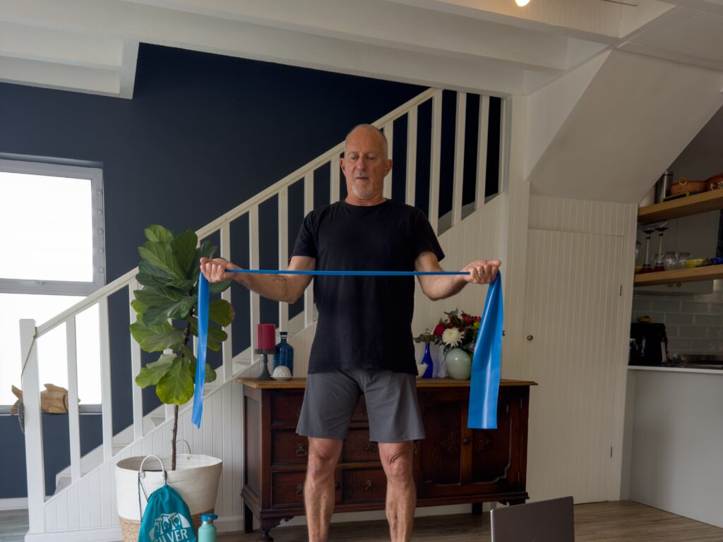 Older adult using a resistance band at home during an online fitness class.
